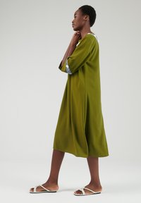 Groene midi-jurk met driekwartmouwen en witte accenten. Glad materiaal, relaxte pasvorm en subtiele zijsplits voor bewegingsgemak.