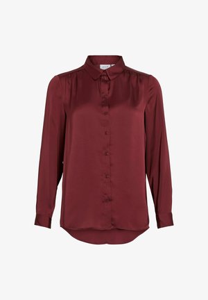 Bordowa bluzka z długimi rękawami wykonana z satynowego materiału, z kołnierzykiem, zapinana na guziki z przodu i lekko marszczonymi ramionami. Zaokrąglony dół.