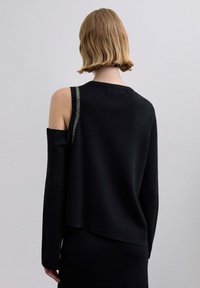 Suéter negro tejido con un diseño único, que presenta un hombro descubierto, un escote redondo y un detalle plateado brillante en la tira.