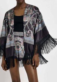 Zwarte satijnen kimono met kleurrijke paisleyprint, franjes langs de randen, gedragen over een zwarte tanktop en bijpassende shorts.