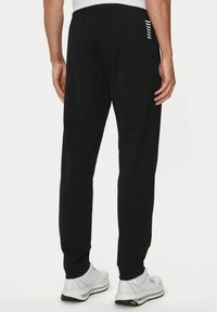 Pantaloni della tuta neri con cintura elastica, gambe leggermente affusolate e accentuazioni a strisce bianche sul lato destro, realizzati in tessuto morbido.