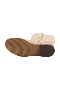 Beige velúr csizma sima felülettel, oldalsó cipzárral és gumi talppal, vízszintes barázdákkal a jobb tapadás érdekében. Lapos sarkú kialakítás.