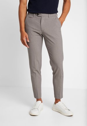 Szare spodnie o dopasowanym kroju noszone z białymi sneakersami i czarnym topem, pokazane od połowy tułowia do stóp na jednolitym tle.