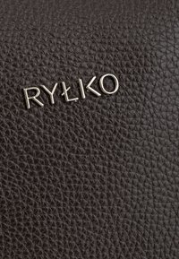 Rudos odos tekstūra su mažu įspaustu sidabriniu logotipu "RYŁKO" ir geometrine rašto fono.