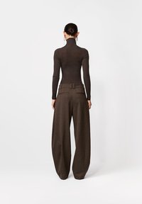 Brązowa dopasowana bluzka z długim rękawem i wysokim kołnierzem w połączeniu z brązowymi spodniami o szerokich nogawkach, wykonanymi z tkaniny o strukturze i ozdobionymi paskiem, widziane od tyłu.
