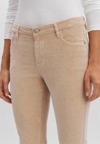 Jeans beige chiaro con una vestibilità slim, realizzati in un morbido tessuto denim. Le caratteristiche includono un classico design a cinque tasche e dettagli in hardware argentato.