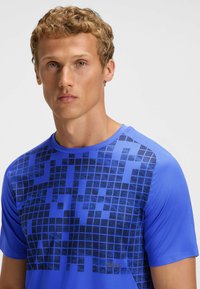 Blå atletisk skjorte med et pixelmønstret mørkeblå design på forsiden. Lavet af letvægtsstof med rund halsudskæring og korte ærmer.