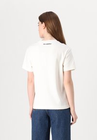 Balta trumpa rankovė t-shirt marškiniai su apvalia iškirpte, ant nugaros esantis juodas "KARL LAGERFELD" logotipas. Lygus medvilnės audinys.