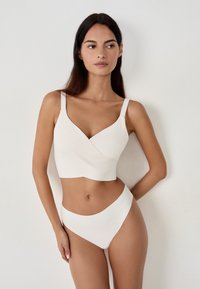 Bralette bianco con design incrociato e spalline sottili abbinato a slip bikini a vita alta. Tessuto liscio, stile minimalista.