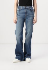 Flared blue jeans with a medium wash, five-pocket design, and a button closure. Features plain hem and light fading along the legs.