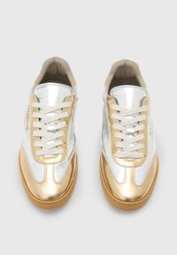 Metallisk sølv- og gullsneaker med kremfargede lisser, med en glatt tekstur, rund form og gummisåle. Merkenavn trykket på siden.