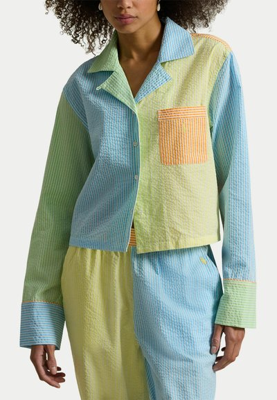 Femme portant un ensemble de pyjama en seersucker rayé pastel avec des panneaux verts, bleus, jaunes et orange, et une poche avant sur la chemise.