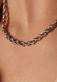 Zilveren gedraaide ketting, met onderling verbonden schakels met een gladde afwerking, rustend op de huid. Geen merkbare patronen of accenten.