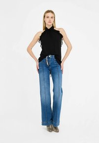 Sort haltertop med flæsekant, kombineret med lyseblå bukser med vide ben og sidesømme. Fodtøjet har et slangeskindsmønster.