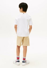 Hvid kortærmet polo shirt og beige shorts, parret med hvide sneakers og sokker med røde, hvide og blå striber, set fra ryggen.