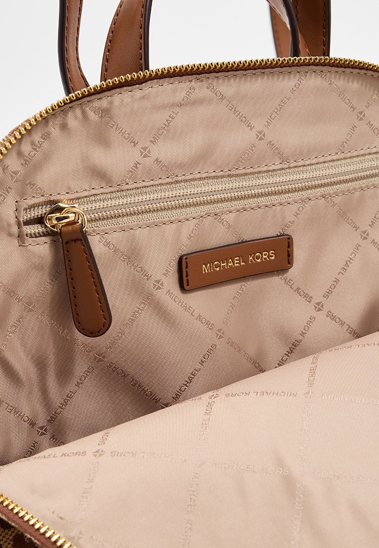 Interno della borsa Michael Kors marrone e beige, con una tasca con cerniera, dettagli del logo su una toppa in pelle e una superficie in tessuto liscio e trapuntato.