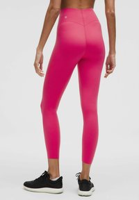 Różowe legginsy z wysokim stanem, wykonane z elastycznego materiału, o eleganckim fasonie. W zestawieniu z czarnymi butami sportowymi dla kontrastu.