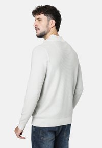 Suéter de punto gris claro con un acabado texturizado, puños acanalados y escote redondo. Combinado con jeans de mezclilla azules.