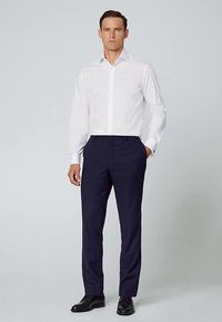 Hvid langærmet skjorte med knaplukket krave kombineret med marineblå bukser. Outfit'et kompletteres med sorte pæne sko.