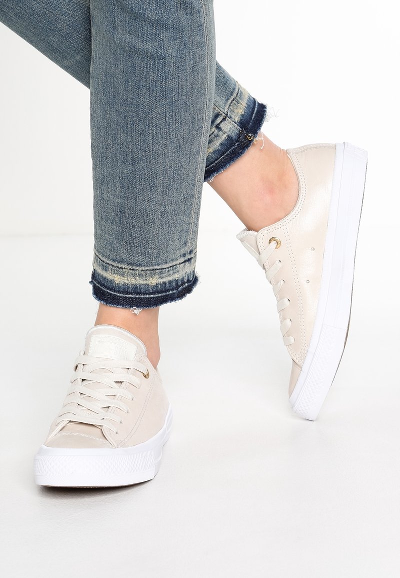 Baskets en toile beige avec semelle en caoutchouc blanche, tige texturée, œillets dorés et lacets plats. Associées à un jean en denim coupé.