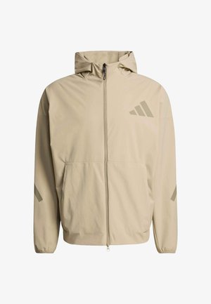 Veste à capuche beige avec une fermeture éclair frontale, deux grandes poches et trois bandes diagonales d'une teinte légèrement plus foncée sur la poitrine et les manches.