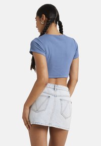 T-shirt bleu coupé, à manches courtes et côtelé, associé à une mini-jupe en denim clair avec deux poches arrière et des coutures visibles.