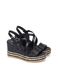 Sandales compensées noires avec des lanières croisées, dessus texturé et semelle en jute tressé. Comprend une boucle réglable au niveau de la cheville et des détails à motif.