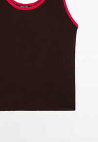 Tummanruskea ribbineulottu toppi, jossa on punainen kaulahihnareunus. Hiuksetön malli ja sileä pinta. Merkin logo näkyy kauluksen läheisyydessä.