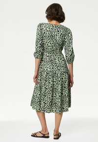 Groene jurk met luipaardprint, korte pofmouwen, een ingesnoerde taille en een gelaagde rok. Gecombineerd met zwarte sandalen met bandjes.