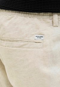 Béžové bavlněné šortky s zadním kapsou, na které je štítek s nápisem "JACK & JONES EST. 1990." Texturovaná látka s jemným povrchem.