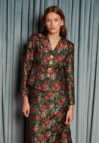 Lillemustriga ülikond läikivast kangast; tumeroheline punaste ja roosade roosidega; sisaldab liibuvat bleiserit kuldsete roosikujuliste nööpidega ja sobivat seelikut.