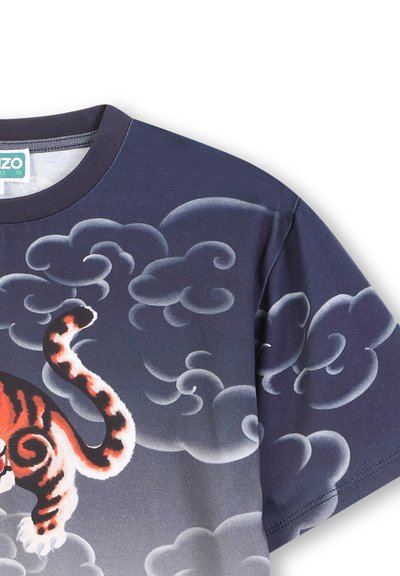 T-shirt bleu foncé avec un graphique de tigre en orange et noir, sur un motif nuageux dans des tons de gris. Matière en coton, design à col ras du cou.