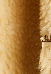 Beige strukturierten Stoff mit einer weichen, flauschigen Oberfläche, die subtile Muster aufweist, und einem kleinen schwarzen Fadendetail am Rand.