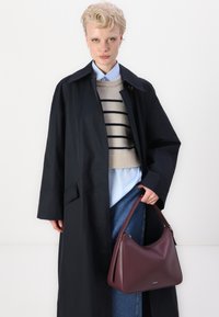 Námornícky trenčkot, béžový pruhovaný svetr, světle modrá košile a džínové kalhoty. Drží vínově červenou koženou kabelku s hladkým povrchem.