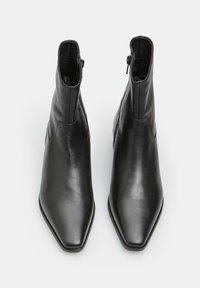 Botas de cuero negro hasta el tobillo con punta afilada, cremalleras laterales y textura suave. La parte superior presenta detalles de costura. Diseño elegante y moderno.