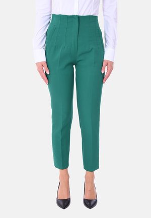 Pantaloni verdi a vita alta con pieghe, gambe affusolate e una texture liscia, abbinati a tacchi neri e una camicia bianca con bottoni.