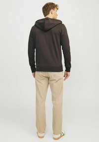 Sudadera negra con capucha ajustable, tejido texturizado, puños acanalados, combinada con pantalones beige claros y zapatos casuales.