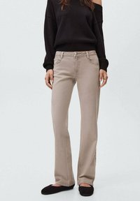 Jeans rectos beige con un diseño clásico de cinco bolsillos, detalles de costura sutiles y una cintura de altura media. Combinados con un suéter negro.