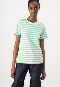 Grønn og hvit stripete kortermet t-skjorte med rund hals, laget av mykt stoff, kombinert med mørke denimbukser.
