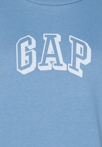 Sudadera de algodón de color azul claro con "GAP" en letras blancas en negrita en el pecho. Textura suave, escote redondo.