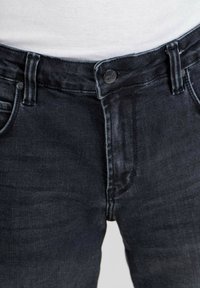 Jeans de mezclilla oscura con un diseño clásico de cinco bolsillos, cierre de botón de metal y patrones de desvanecimiento sutiles a lo largo de la tela.