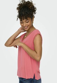 Lyserosa bluse med en myk tekstur, scalloped blondedetaljer på ermene, løs passform og sidespalter. Brukt med blå jeans.