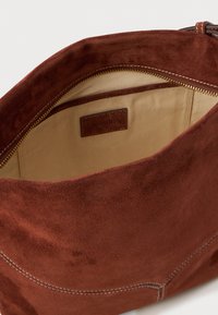 Borsa a tracolla in suede marrone con chiusura a zip, dotata di una fodera interna beige e di una piccola etichetta del brand. Design semplice e funzionale.