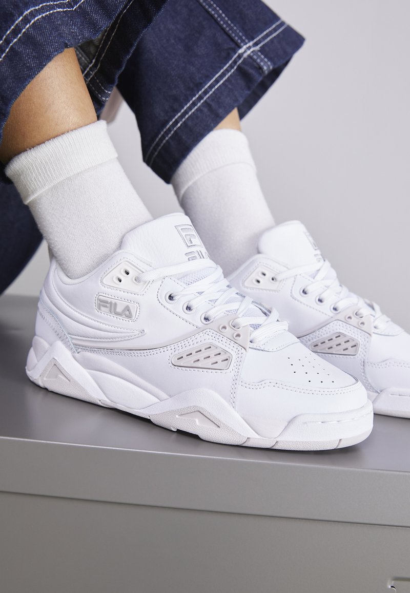 Sneakers atletiche bianchi con upper in sintetico testurizzato, dettagli in mesh e design perforato. Presentano una suola robusta con dettagli angolari.