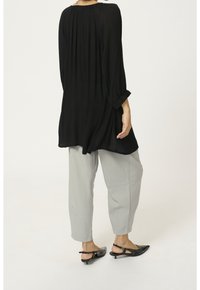 Tunique noire à manches longues avec une coupe ample, dotée d'un dos plissé, associée à un pantalon gris clair effilé et des chaussures noires à talon ouvert.