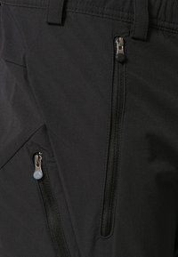 Pantalons d'extérieur noirs avec deux poches zippées, tissu texturé et taille ajustée. Les zippers sont métalliques avec des languettes contrastées.