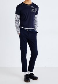 Marinblå kortärmad skjorta med randiga långärmar, nummer "24" i grått, tillsammans med marinblå byxor och svarta skor.