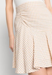 Saias de padrão gingham em bege e branco, com um cós franzido, bainha evasê e tecido leve que oferece uma aparência texturizada.