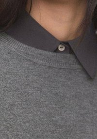 Pull gris avec un col foncé, présentant un col côtelé et des détails à boutons sur le col, fabriqué en tissu doux et texturé.