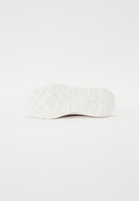 Biała podeszwa sportowego buta z teksturowanym, wielokierunkowym wzorem bieżnika zapewniającym lepszą przyczepność i trakcyjność.